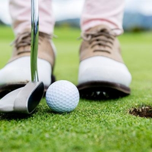 Closeup of a golfer's shoes, putter and golf ball on the greens